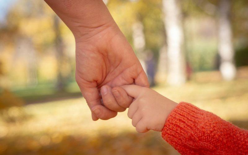 męska ręka trzyma palec małej rączki dziecka symbolizując opiekę