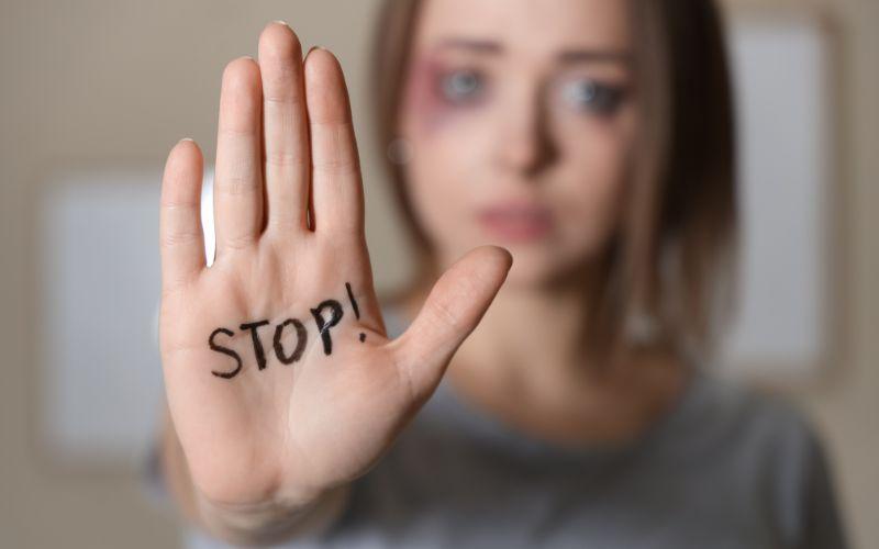 Kobieta z podbitym okiem i napisem „STOP!” na dłoni.