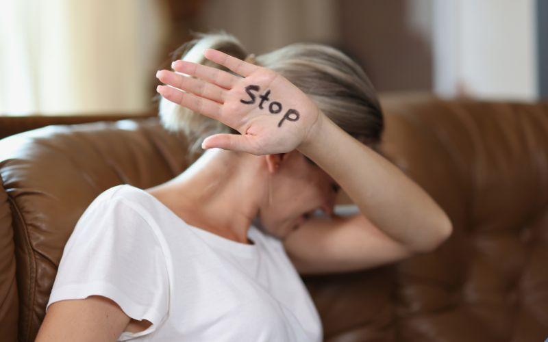 Kobieta zasłaniająca twarz dłonią z napisem STOP – symbol sprzeciwu wobec przemocy domowej